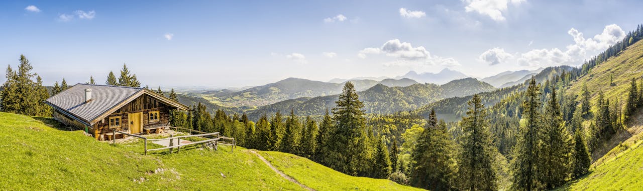 Idyllic alpine landscape with a rustic cabin amidst lush greenery and mountain backdrop in Germany.
